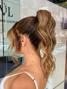 A woman with long hair in a high ponytail from curly blowdry in front of Vlushe Lounge